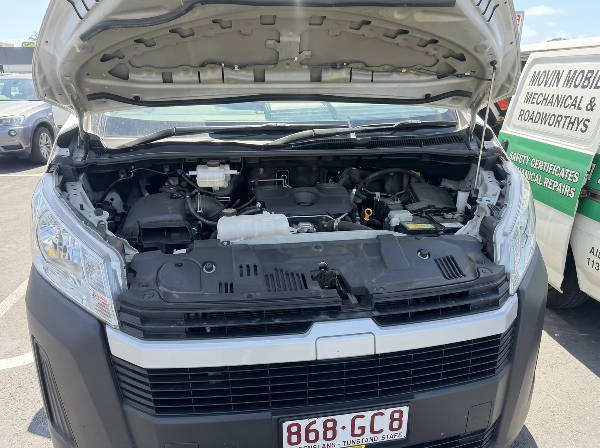 Open engine bay of a vehicle parked beside a Movin Mobile van